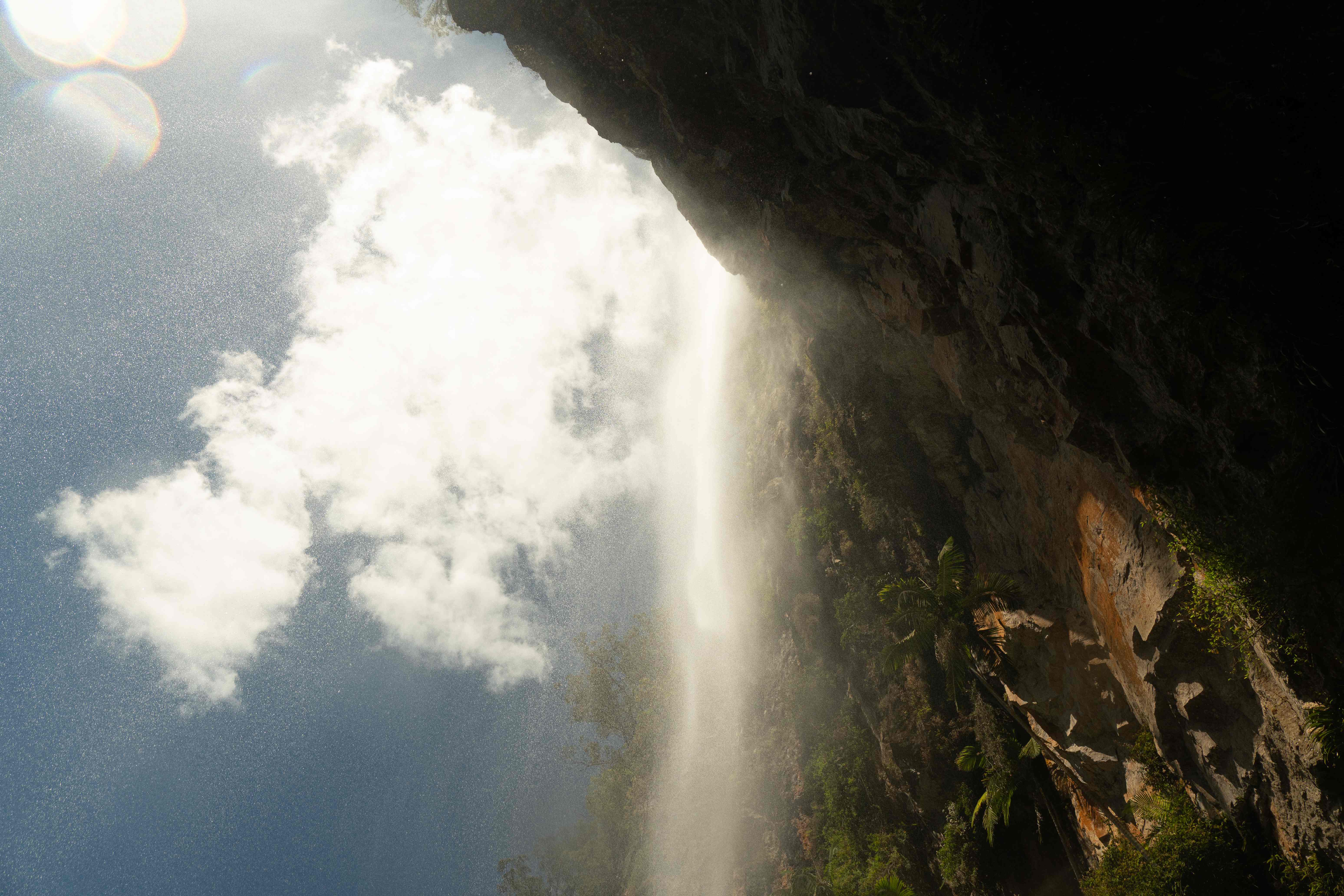 Waterfall spilling over a sunlit rainforest cliff